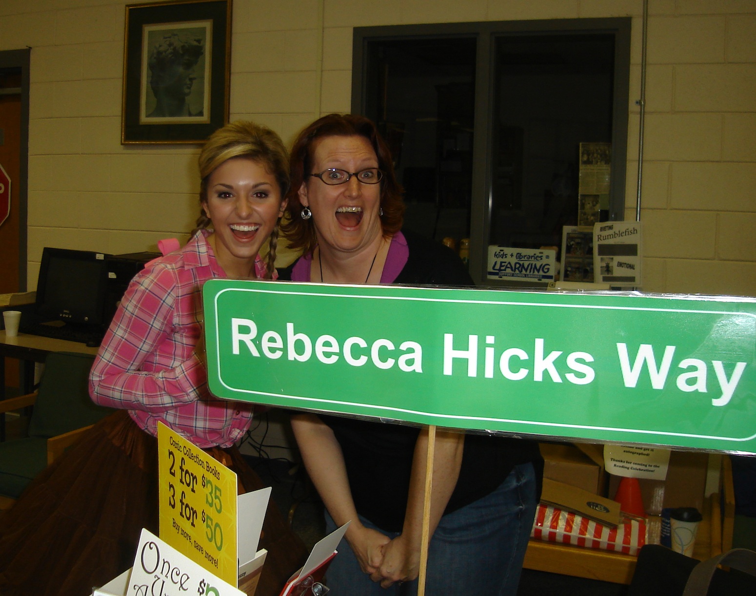 Photo of Haley Wheeler and Rebecca Hicks posing behind a sign that reads “Rebecca Hicks Way”