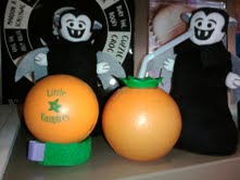 Two Little Vampire plush toys pose behind a blood orange stress ball and an orange-shaped juice sipper.