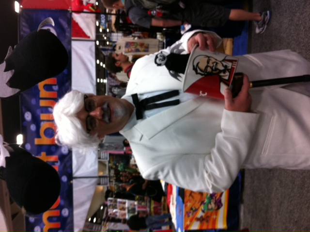 Man wearing Colonel Sanders cosplay and posing with a Little Vampires plush toy