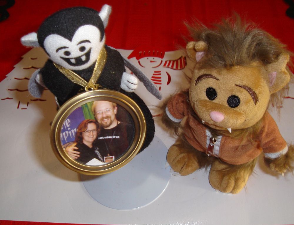 Photo of a Little Vampire plush toy and a Wolfie plush toy. The Little Vampire is wearing a framed photo of Rebecca and James Hicks around his neck.