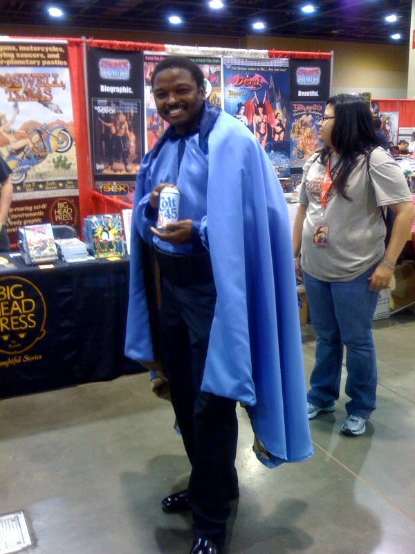 Man in Lando Calrissian cosplay, smiling and displaying a can of Colt 45 Malt Liquor