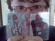 Photo of Little Vampires fan Nicholas holding up two sketch cards by Rebecca Hicks. A weeping angel wearing a fez is on the left, and the TARDIS wearing a fez is on the right.