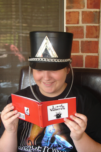 Hannah, a teenage girl, wears a black cadet hat while reading the Little Vampires book.