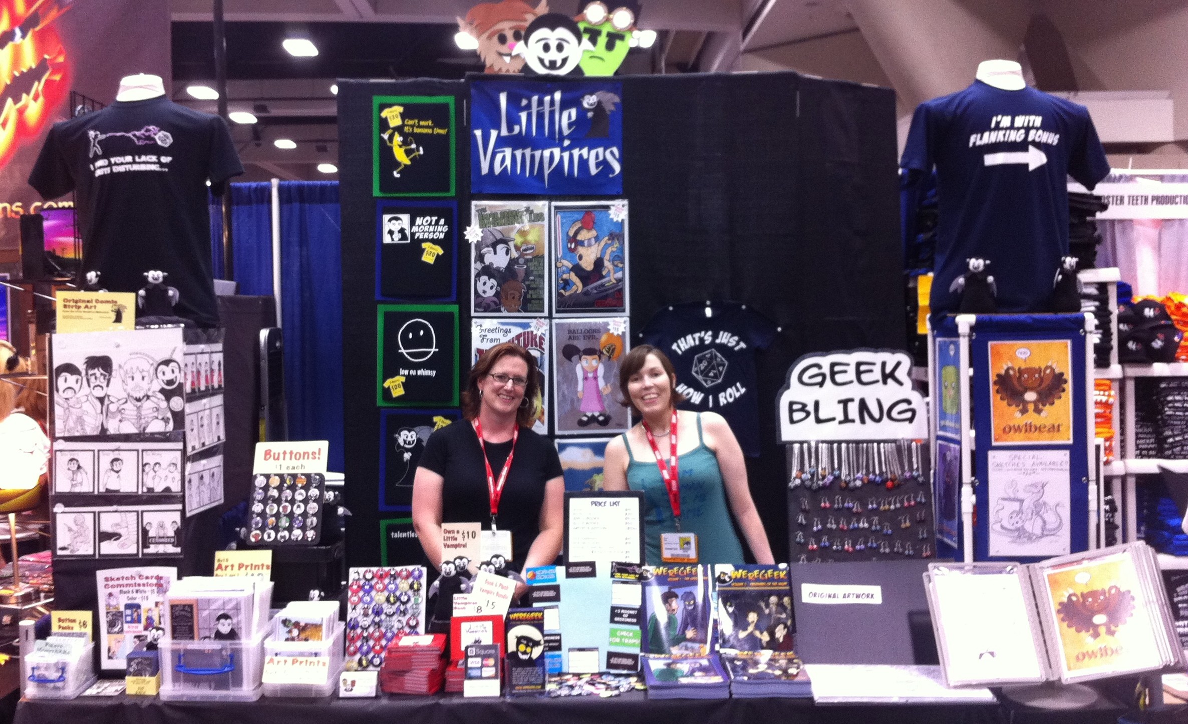 Photo of Rebecca Hicks and Alina Pete standing in the shared Little Vampires and Weregeek booth at San Diego Comic-Con 2011