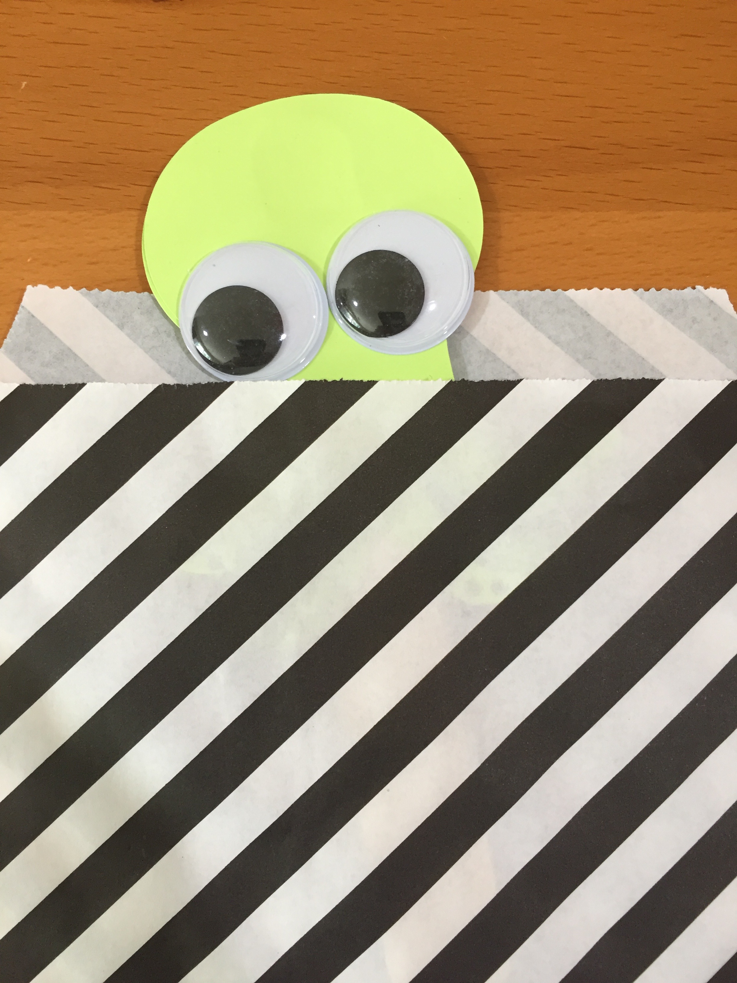 Photo of a googly-eyed monster peeking out of a zebra-striped paper bag