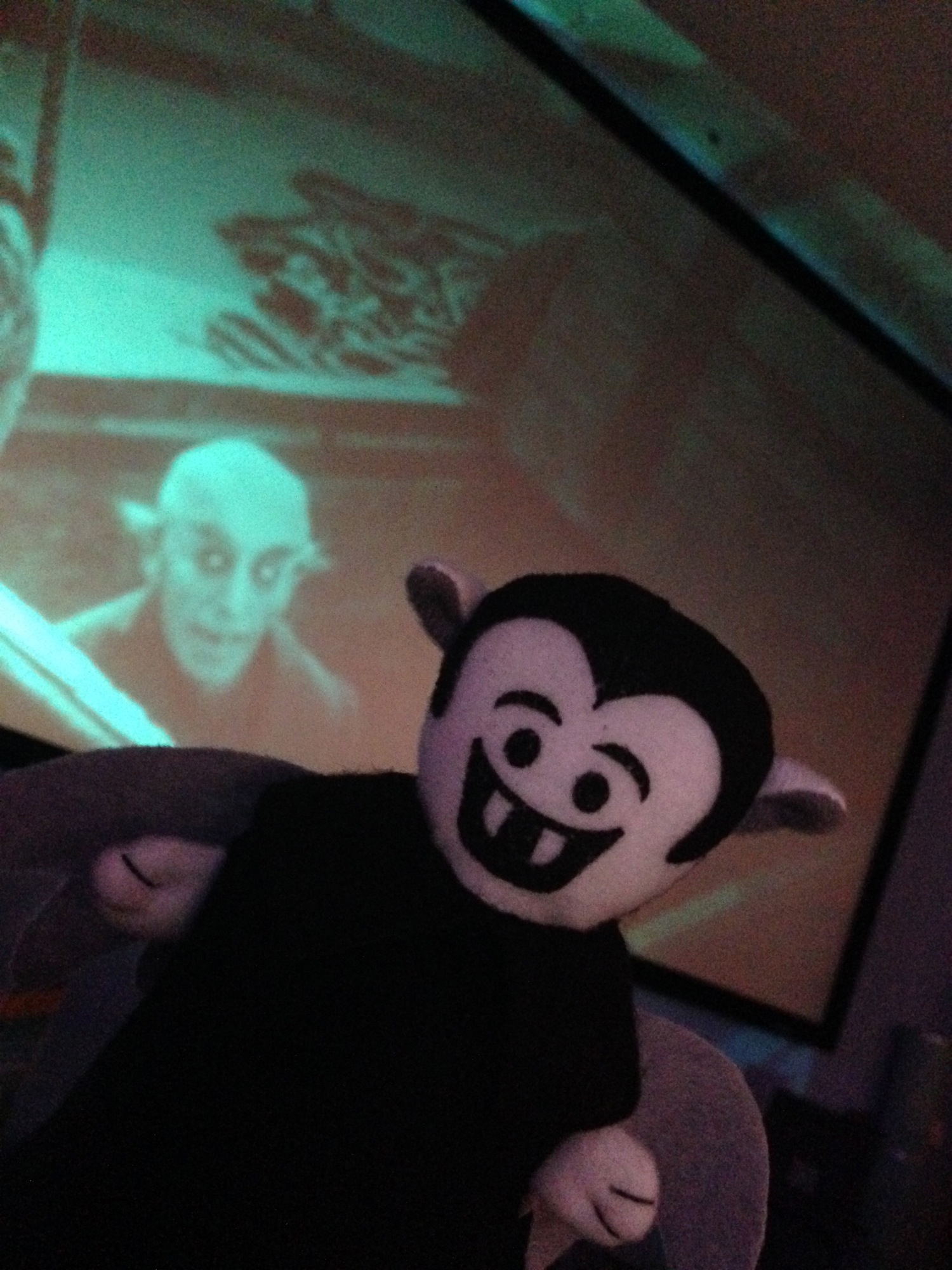 Photo of a Little Vampire plush toy posing in front of a screen showing Nosferatu