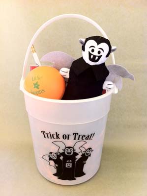 Glow-in-the-dark Halloween bucket depicting the Little Vampires, captioned “Trick or Treat!” Contents are a Little Vampires plush toy, blood orange stress ball, Little Vampires hardcover book, and a Little Vampires wooden pencil.